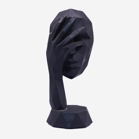 A surreal sculptural artwork depicting a reddish human head and hands merged with a long, weathered wind instrument. The figure appears to be playing the instrument, which extends horizontally across the image. The piece has a rustic, textured finish and